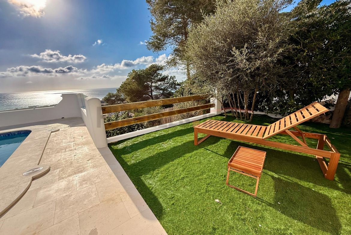 Tumbona de madera en césped artificial junto a la piscina con vistas al mar en una villa de lujo en Menorca.