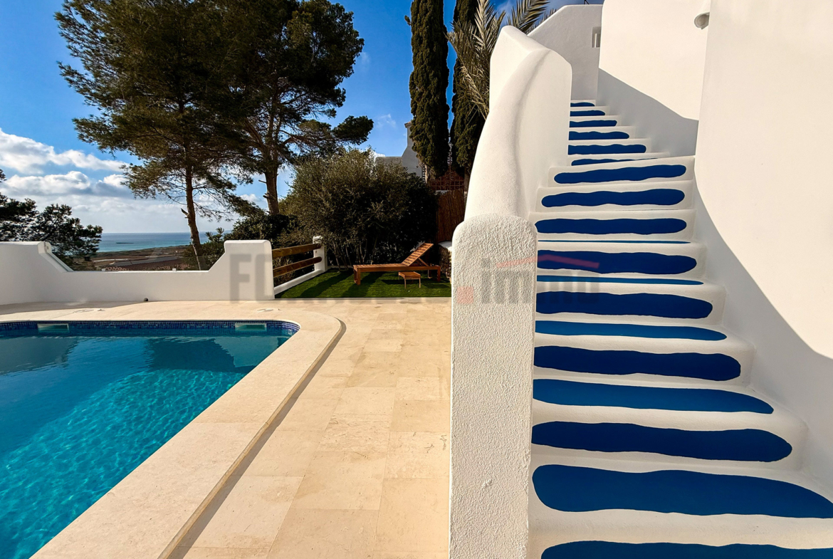 Escaleras blancas con escalones azules vibrantes junto a una piscina y vistas al mar en villa de lujo en Menorca.