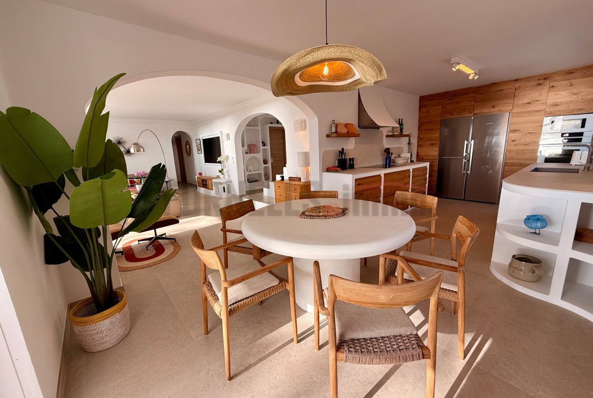 Amplia cocina y comedor de concepto abierto con isla, mesa redonda, sillas de madera, y decoración moderna en villa de lujo en Menorca.