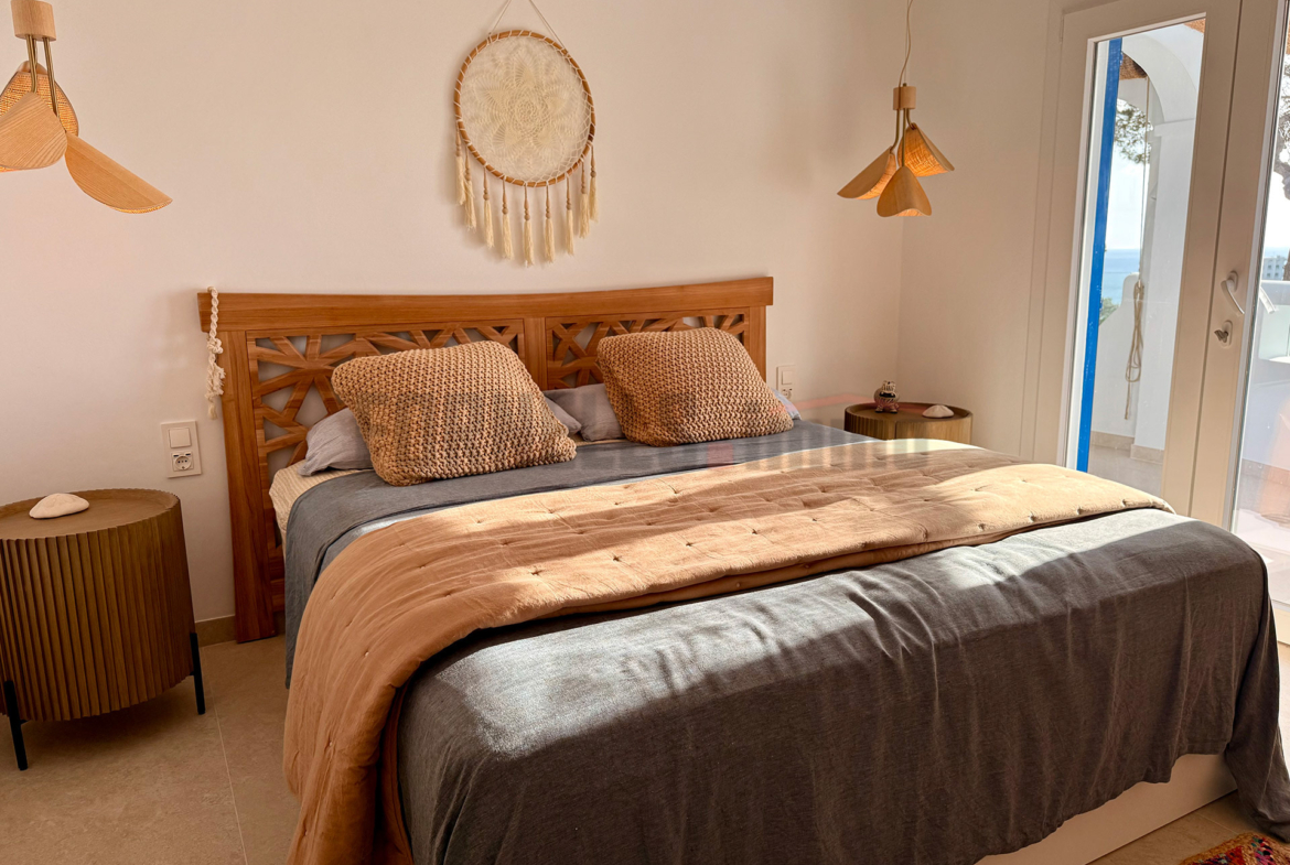 Dormitorio doble con cama de madera, textiles naturales, y acceso a terraza con vistas en villa de lujo en Menorca.