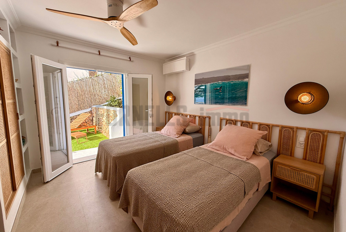 Dormitorio con dos camas individuales, ventilador de techo, armario de rejilla y acceso a jardín privado en villa de lujo en Menorca.