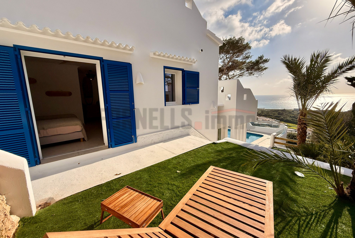 Terraza privada con césped artificial, tumbona de madera y vistas al mar en una villa de lujo en Menorca.