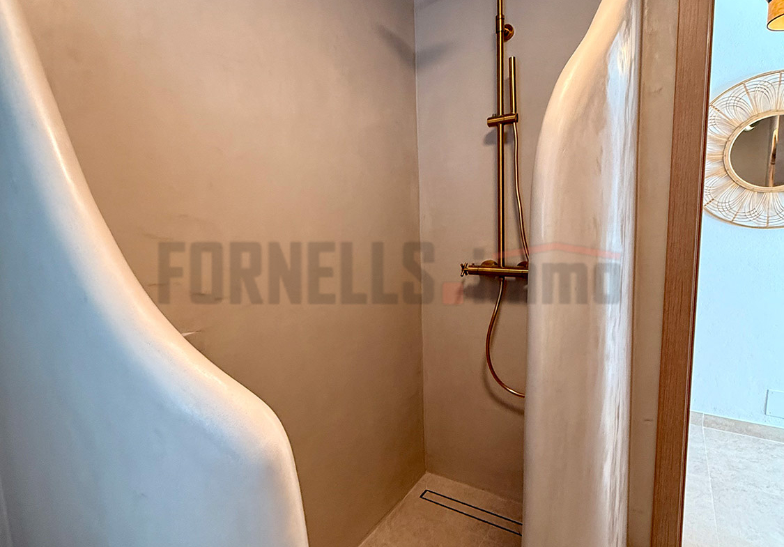 Ducha sin puerta con diseño curvilíneo, grifería dorada y nicho, integrada en el baño de una habitación de lujo en Menorca.