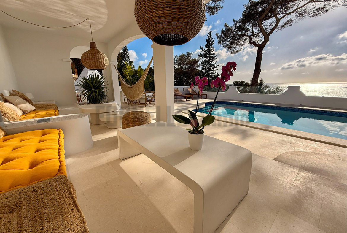 Terraza cubierta con sofás, mesa de centro, piscina y vistas al mar en esta villa de lujo en Menorca.